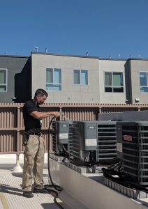 HVAC Tech washing a condenser unit with a water hose