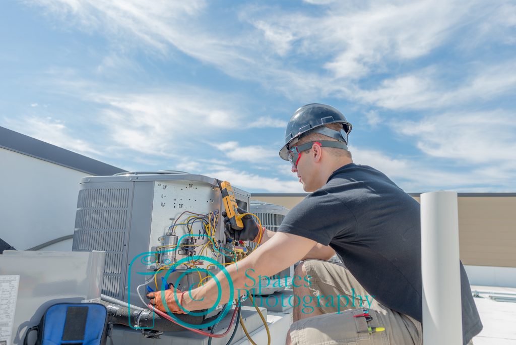 Hvac tech working on a condensing unit rooftop, holding a volt meter adjusting a temperature clamp. 