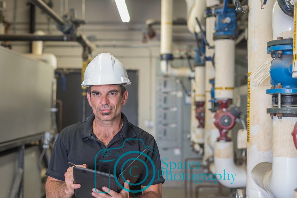 Hvac Technician writing on a tablet, standing in a boiler room. 