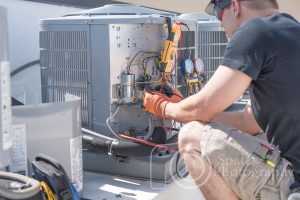 Hvac repair technician using a volt meter to test components on an air conditioner condenser.