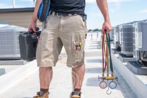 Hvac technician holding refrigerant gauges with condensers in view