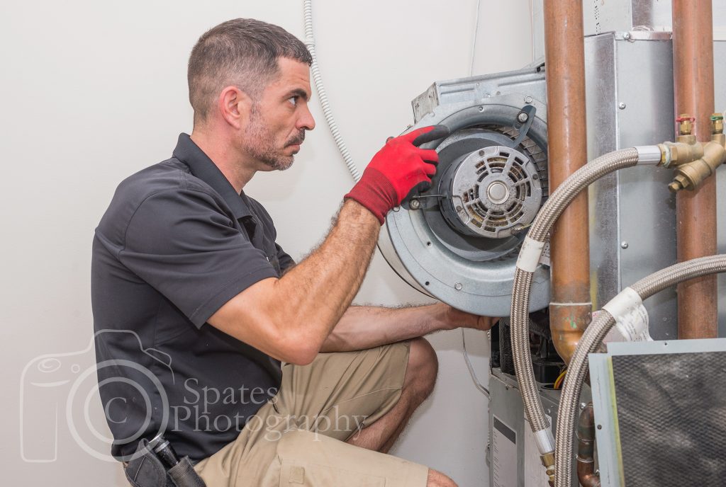 HVAC technician removing a furnace blower motor from a commercial heat pump. Repair man wearing a uniform and safety gloves.