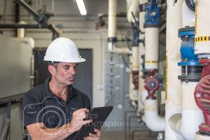 HVAC/R technician writing on a tablet, standing in a boiler room